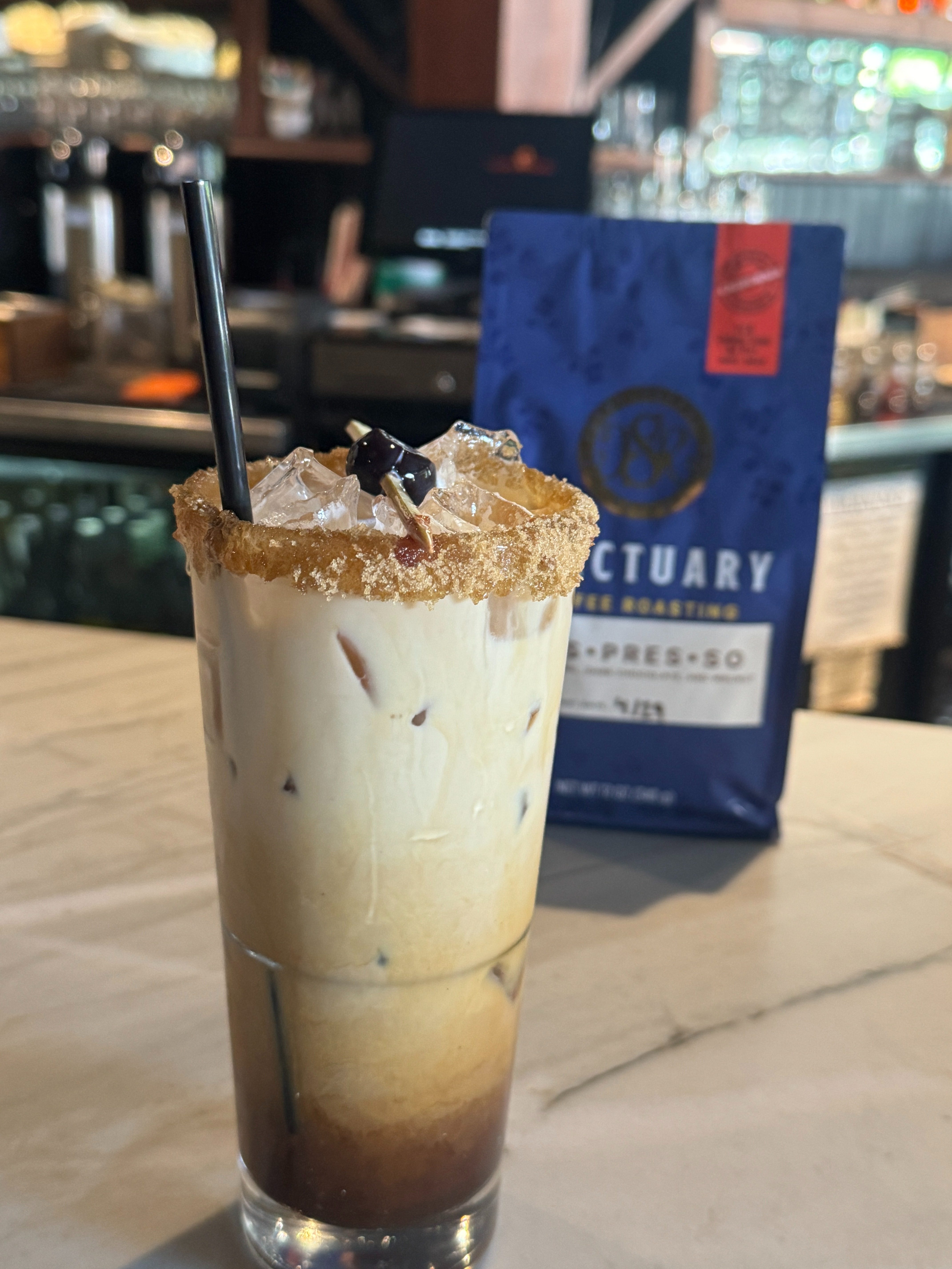 Iced espresso drink beside a bag of Sanctuary Roasting coffee